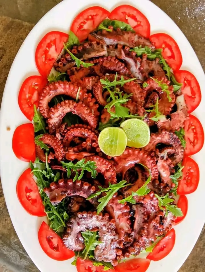 Grilled octopus on a platter with sliced tomatoes, herbs and lime