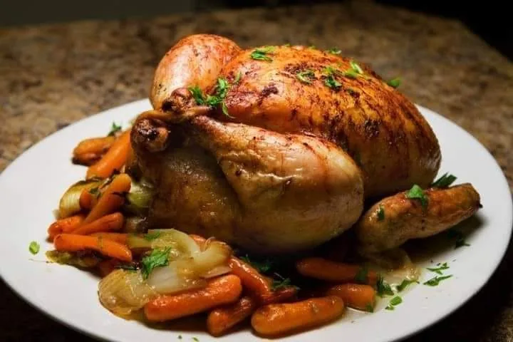 A whole roast chicken served with carrots and other vegetables