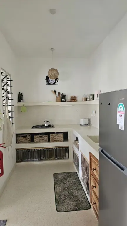 Narrow bright kitchen with hob, counters, woven storage baskets and refrigerator