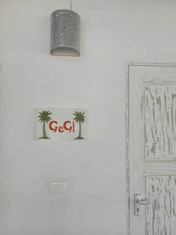 Painted GeGi sign with two palm trees on a white wall beside a weathered door