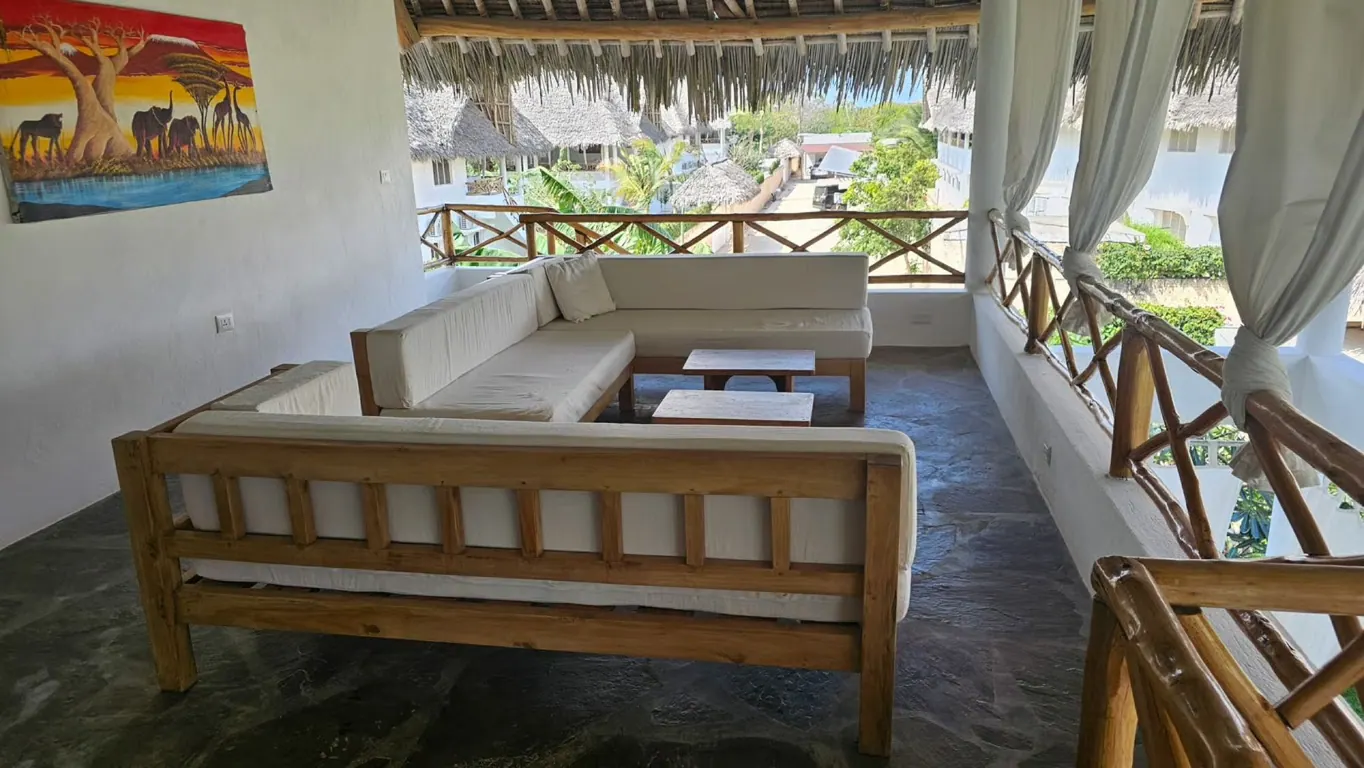 Open-air terrace lounge with wooden sofas, white cushions and tropical rooftops beyond