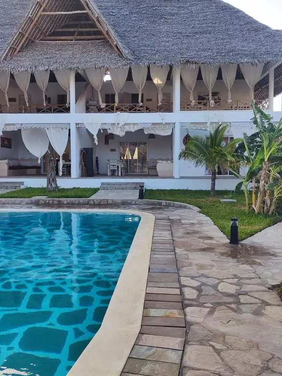 Curved edge of the shared pool facing an open-front white thatched building