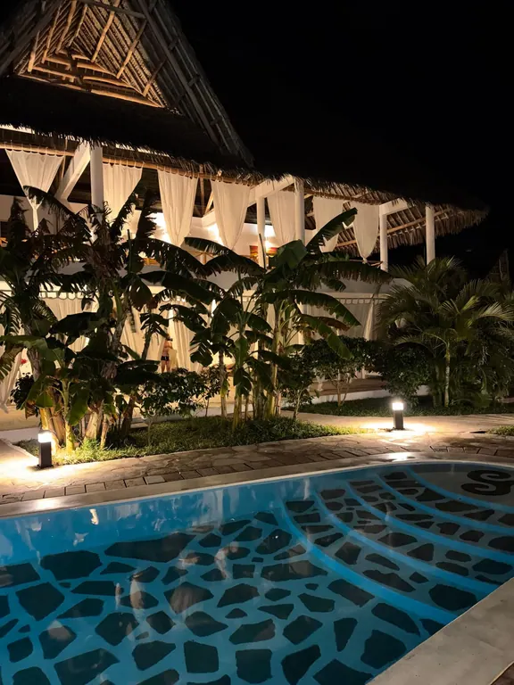 Illuminated thatched building and patterned shared pool at night
