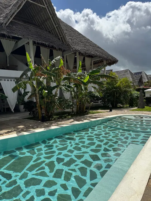Curved shared pool beside banana trees and a white thatched building