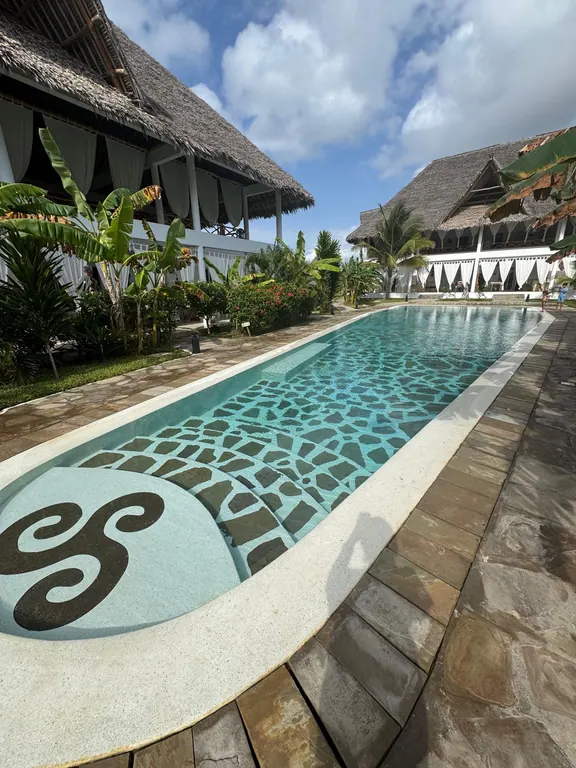Wide shared pool between white thatched buildings beneath a bright sky