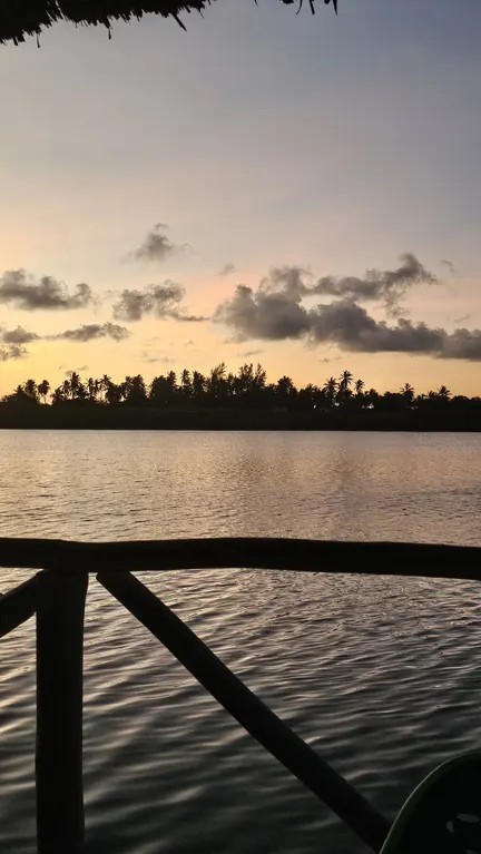 Dusk across calm water framed by a thatched roof and rustic railing
