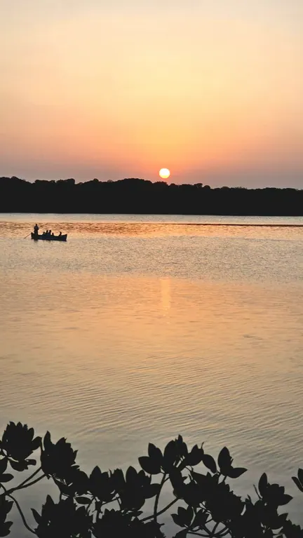 Orange sunset over calm water with a small boat and distant tree line