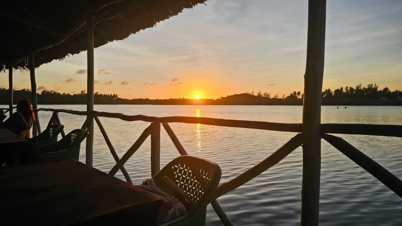 Sunset over calm water viewed from a covered wooden deck with seated people