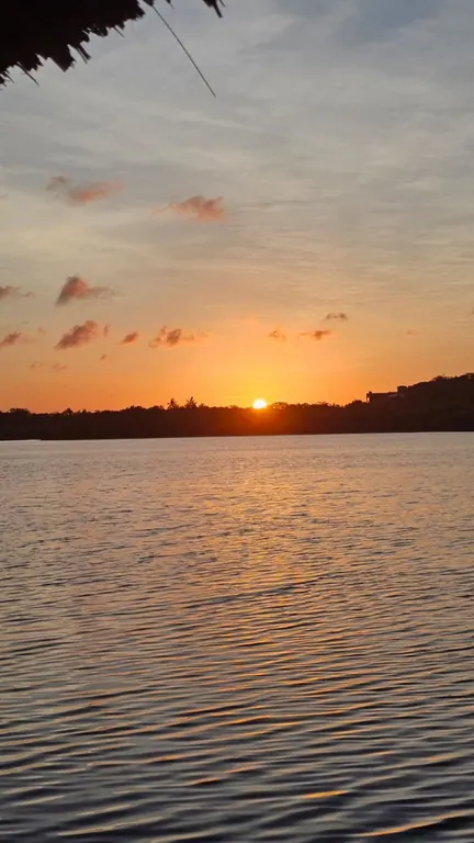 Low orange sunset reflected across calm water below a cloudy sky