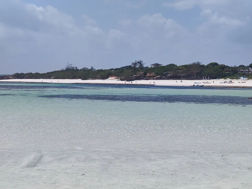 Shallow turquoise water facing a white beach and green shoreline