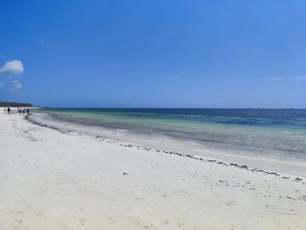 Wide white-sand beach beside blue and turquoise ocean under a clear sky