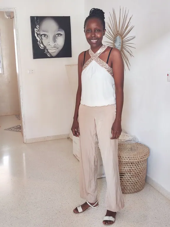Smiling woman in a white top and beige trousers standing in a bright interior